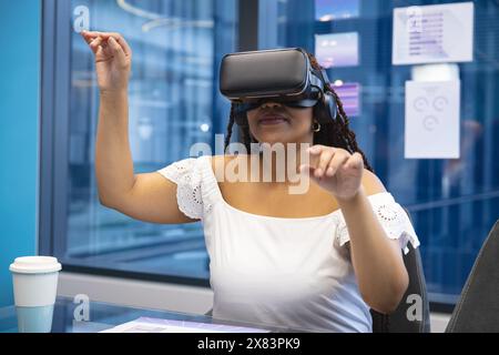 In modernen Geschäftsbüros trägt eine junge, birassische Frau ein Virtual-Reality-Headset Stockfoto