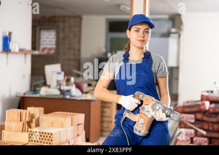 Bauherrin in blauen Overalls, die auf der Baustelle mit Meißelhammer steht Stockfoto