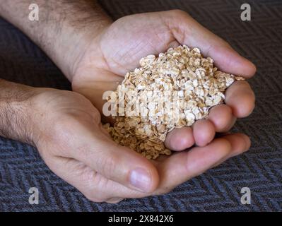 Nahaufnahme von Händen eines jungen Mannes, der Haferflocken von einer Hand in die andere fällt. Grauer Hintergrund. Gesunde Ernährung. Vegan Stockfoto