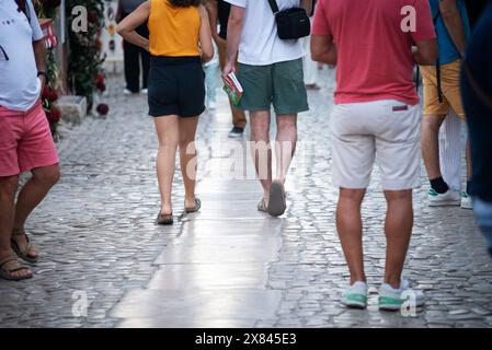 Rua Direita, Óbidos, Portugal. Sandelbedeckte Touristen mit Reiseführer in der Hand auf der kopfsteingepflasterten Rue Direita, der Hauptstraße der Stadt aus dem 13. Jahrhundert, die von der Porta da Vila (Haupteingang der Stadt) bis zur Burg von Óbidos (Pousada do Castelo de Óbidos) führt. Stockfoto