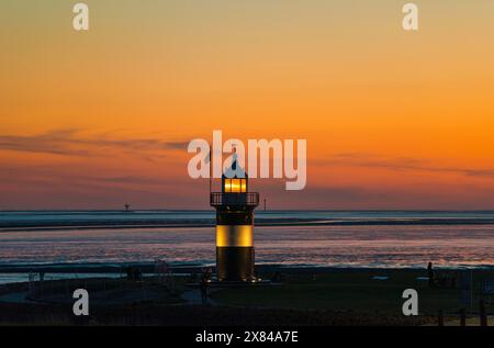 Der schwarz-weiße Leuchtturm „kleine Preusse“ steht kurz nach Sonnenuntergang, Abenddämmerung vor einem orangefarbenen Himmel an der Küste Stockfoto