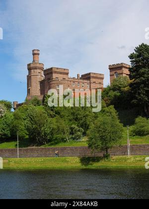 Historisches Schloss mit Backsteintürmen auf einem grünen Hügel, am Ufer eines Flusses unter blauem Himmel, Schloss mit Turm am Fluss mit grünen Bäumen Stockfoto