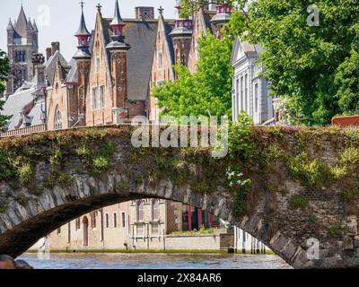 Steinbrücke über einen Kanal mit historischen Türmen und Gebäuden im Hintergrund, umgeben von grünem Laub, alten historischen Hausfassaden mit Türmen Stockfoto