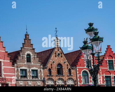 Historische Backsteingiebelhäuser auf einem Platz unter klarem blauen Himmel, mit einer dekorativen Straßenlaterne im Vordergrund, alte historische Häuser mit Kirche Stockfoto