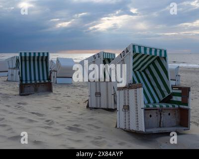 Mehrere leere Liegen mit grünen und weißen Streifen stehen am Sandstrand, der Himmel ist bewölkt, bunte Liegen am Strand in Stockfoto