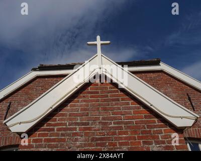 Kirchendach mit weißem Kreuz auf rot gekacheltem Dach an klarem blauem Himmel, kleine Kirche mit historischem Glockenturm auf einer Insel, Baltrum, Deutschland Stockfoto