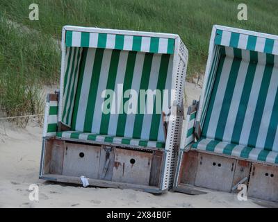 Zwei grün gestreifte Liegestühle stehen nebeneinander an einem Sandstrand vor Dünen, bunte Liegen am Strand vor Dunkelheit Stockfoto