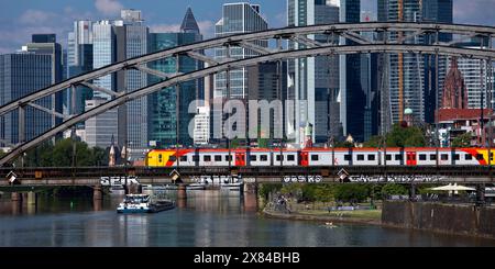 Main mit Regionalbahn auf der Deutschherrnbrücke und einem Frachtschiff vor der Skyline von Frankfurt am Main, Hessen Stockfoto