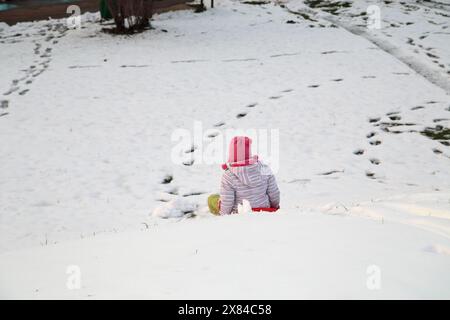 Ein Kind auf einem Schlitten geht eine Schneerutsche hinunter. Nahaufnahme. Stockfoto