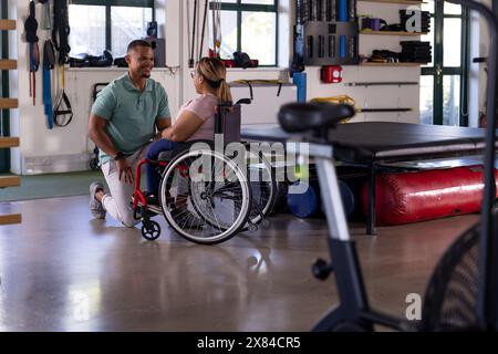 Eine birassische Querschnittsgelähmte Patientin im Rollstuhl spricht mit ihrer Therapeutin im Reha-Zentrum Stockfoto