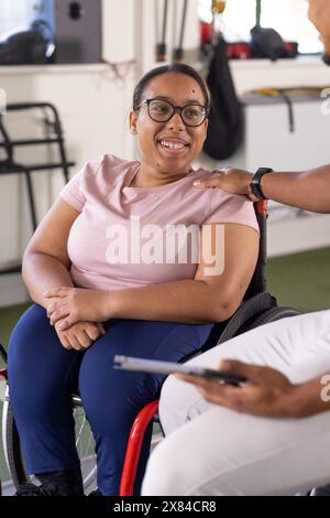 Eine birassische Querschnittsgelähmte Patientin im Rollstuhl in einem Reha-Zentrum im Fitnessstudio, lächelnd Stockfoto