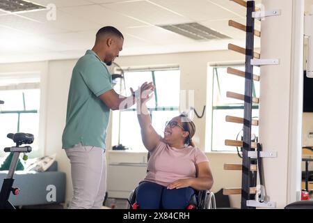 Im Reha-Zentrum in der Turnhalle hilft birassischer männlicher Therapeut birassischer weiblicher Querschnittsgelähmter Stockfoto