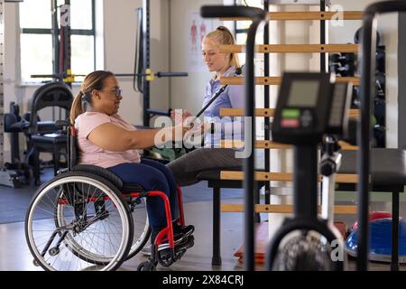 Im Reha-Zentrum des Fitnessstudios unterhalten sich birassische Querschnittslähmung und kaukasische Therapeutin Stockfoto