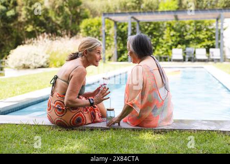Im Freien unterhalten sich verschiedene ältere Freundinnen am Pool Stockfoto