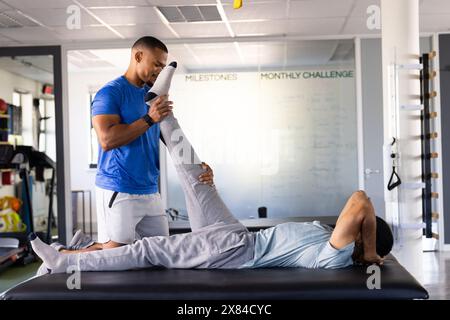 Im Rehabilitationszentrum hilft birassischer Physiotherapeut Patienten mit Beinübungen Stockfoto