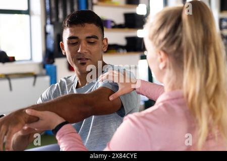 Im Rehabilitationszentrum hilft eine kaukasische Physiotherapeutin birassischen männlichen Patienten Stockfoto