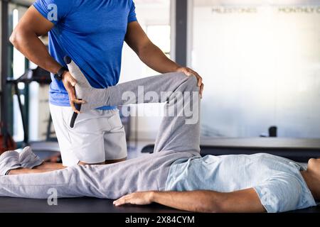 Birassischer Therapeut und Sportbekleideter machen Beinübungen im Rehabilitationszentrum Stockfoto