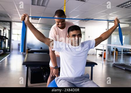 Im Rehabilitationszentrum behandelt birassischer männlicher Physiotherapeut Patienten, beide in Sportbekleidung Stockfoto