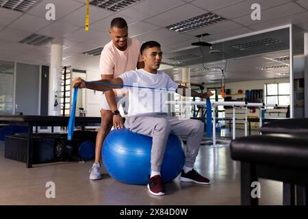 Im Rehabilitationszentrum behandelt birassischer männlicher Physiotherapeut Patienten, beide in Sportbekleidung Stockfoto