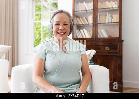 Ältere asiatische Frau, die während eines Videoanrufs zu Hause sitzt und in einem hellen Raum lächelt Stockfoto