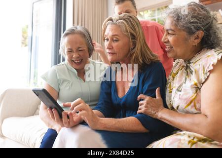 Verschiedene ältere Freundinnen, die zu Hause lachen und sich ein Tablet ansehen Stockfoto