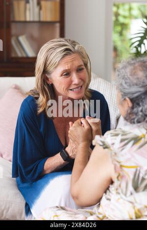 Verschiedene ältere Freundinnen sitzen, reden zu Hause mit blauem Hintergrund Stockfoto