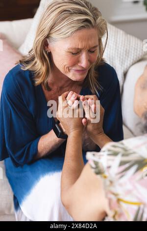 Verschiedene ältere Freundinnen halten zu Hause Hände und zeigen Unterstützung Stockfoto