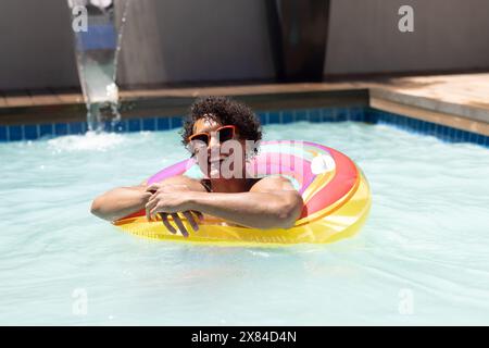 Ein birassischer junger Mann, der sich im Freien entspannt und farbenfrohe Schwimmer hält Stockfoto