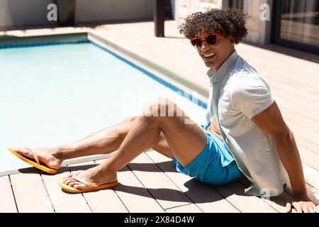 Ein birassischer junger Mann mit Sonnenbrille, entspannte sich draußen am Pool Stockfoto