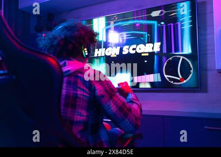 Ein birassischer junger Mann, der zu Hause Videospiele spielt, mit kariertem Hemd Stockfoto