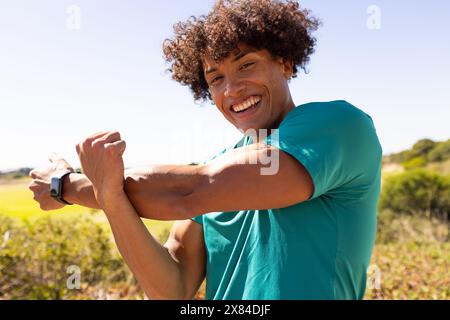 Ein birassischer junger Mann, der ein grünes Hemd trägt und sich draußen ausdehnt Stockfoto