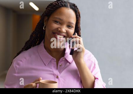 Junge Frau mit geflochtenen Haaren lächelt am Telefon in einem modernen Büro für Geschäftsleute Stockfoto