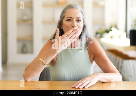 Zu Hause, reife kaukasische Frau, die während eines Videogesprächs den Mund bedeckt Stockfoto