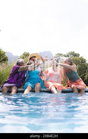 Am Pool lachen verschiedene ältere Freundinnen, toasten Getränke, Kopierraum Stockfoto