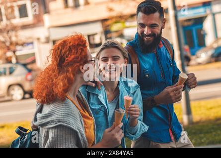 Eine Gruppe von Touristen genießt den Urlaub, junge Freunde, die Spaß haben, auf der Stadtstraße zu spazieren und Eis während des Sonnenuntergangs zu essen. Stockfoto