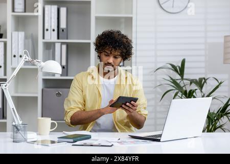 Junge Profis, die am Schreibtisch in einem modernen Büro arbeiten, mit Laptop und Taschenrechner, umgeben von Papieren. Konzentriert sich auf die Verwaltung von Geschäftsaufgaben. Stockfoto