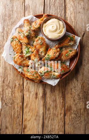 Hausgemachte, gebratene Parmesan Chicken Wings mit Dipping Sauce aus nächster Nähe auf dem Teller auf dem Tisch. Vertikale Draufsicht von oben Stockfoto