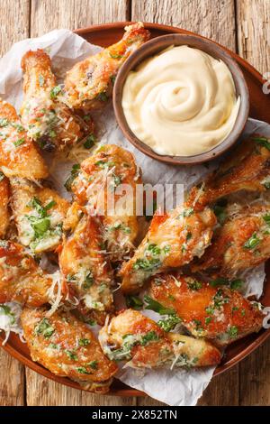 Knusprige Petersilie Knoblauch Käse Chicken Wings serviert mit Dipping Sauce in Nahaufnahme auf einem Teller auf dem Tisch. Vertikale Draufsicht von oben Stockfoto