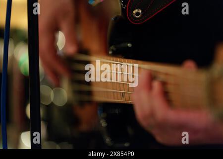 Nahaufnahme von Fingern, die am Griffbrett der Bassgitarre Saiten drücken – warme Beleuchtung fängt musikalische Präzision und Stimmung ein. Stockfoto