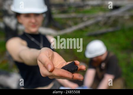 Schierke, Deutschland. Mai 2024. Sarah Götz, Geographiestudentin an der Gerog-August-Universität Göttingen, zeigt in einem Wald bei Schierke ein Stück Kohle, das aus einem Holzkohleofen stammt, den einst ein Holzkohlebrenner dort betrieben hat. Der Student untersucht das Gelände in der Quesenbank/Knaupsholz. Der Wald brannte dort vom 11. August 2022 bis zum 14. August 2022 ab. Quelle: Klaus-Dietmar Gabbert/dpa/Alamy Live News Stockfoto