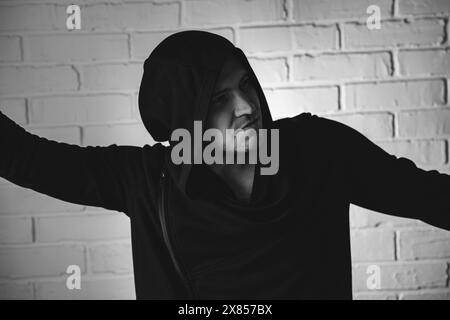 Ein Mann, der einen schwarzen Hoodie trägt, tanzt energisch mit ausdrucksstarken Handbewegungen vor einer weißen Ziegelwand. Stockfoto