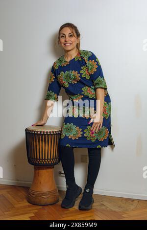 Eine Perkussionistin, Erwachsene lateinische Frau, posiert mit ihrer Djembe-Trommel zu Hause. Vorstellung von Freude und Feier, während die Frau lächelt und h genießt Stockfoto