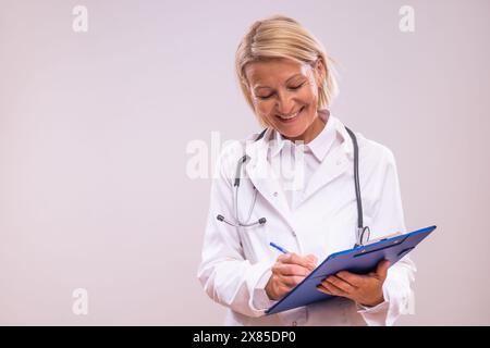 Porträt einer reiferen Ärztin, die Notizen auf grauem Hintergrund schreibt. Stockfoto