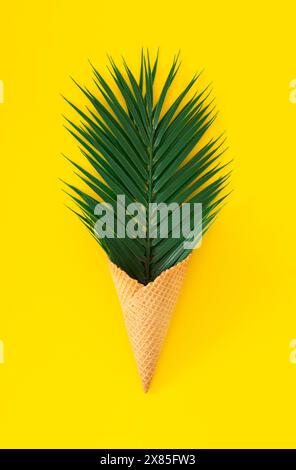 Grüne Palmenblätter in Eiskegel auf hellgelbem Hintergrund. Trendiges tropisches Konzept. Minimales Design für den Sommer. Exotische flache Lage. Stockfoto