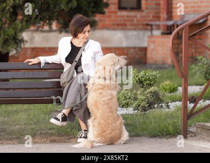 Junge Frau Sitzt Im Frühling Auf Der Bank In Der Nähe Von House Mit Golden Retriever Stockfoto