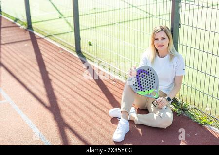 Ukraine Kiew, 03. Mai 2024. Porträt einer lächelnden Frau mit Padel-Tennisschlägerkopf auf dem Hof Stockfoto