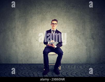 Ein Bewerber, ein junger Geschäftsmann, der auf einem Stuhl sitzt und ein Bewerbungsformular ausfüllt Stockfoto