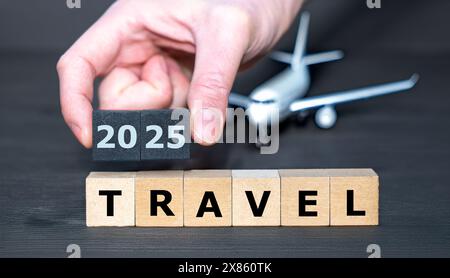 Holzwürfel bilden den Ausdruck „Travel 2025“ vor einem Modellflugzeug. Symbol für Urlaub im Jahr 2025. Stockfoto