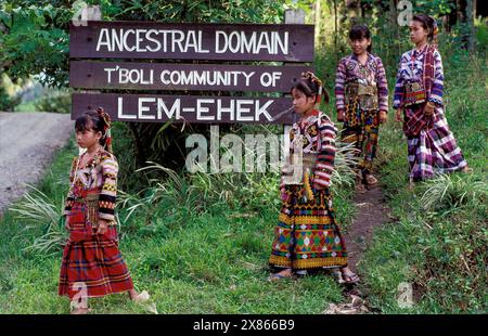 Philippinen, Mindanao; Mädchen aus dem Stamm der T'boli gehen vor dem Schild „Ahnenstamm“ in der Nähe ihres Dorfes. Stockfoto