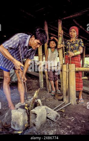 Philippinen, Mindenao; Bronzestatuen eines Mannes aus dem Stamm der Tboli werden in einem Feuer erhitzt, das seine Frau mit einem Bambusbalg hält. Stockfoto